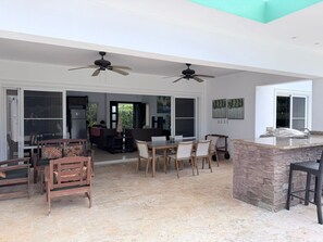 Ampla sala de estar com mesa de jantar, cadeiras, ventiladores de teto e parede de pedra decorativa.