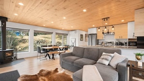 A modern living room with a grey sofa, a wooden ceiling, and a large window overlooking a garden.