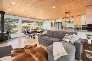 A modern living room with a grey sofa, a wooden ceiling, and a large window overlooking a garden.
