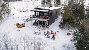 Een moderne blokhut met een balkon, omgeven door sneeuw en bomen.