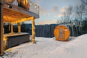 Een houten vakantiehuisje met balkon en hottub, omringd door sneeuw en bomen.