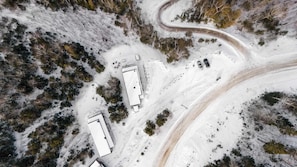 Luchtbeeld van een besneeuwd gebied met een kronkelende weg, meerdere gebouwen en geparkeerde auto's.