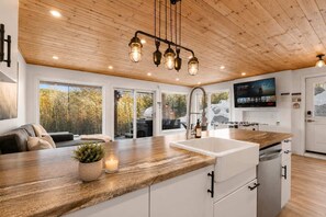 A modern kitchen with a wooden ceiling, a large window, and a built-in dishwasher.