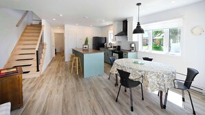 Una cocina moderna con una isla central, una escalera de madera y un comedor con mesa y sillas.