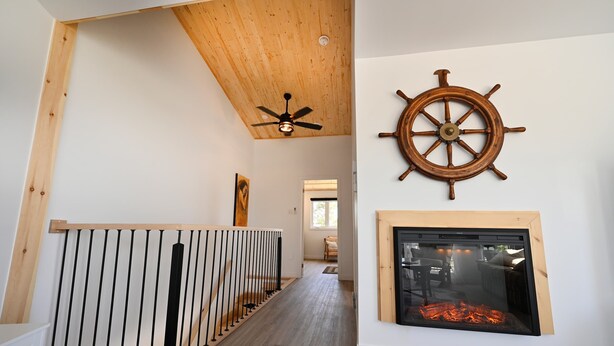 Un pasillo con techo de madera, ventilador de techo, timón de barco y chimenea.