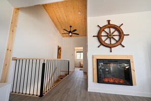Un couloir avec un plafond en bois, un ventilateur de plafond, un gouvernail de bateau et une cheminée.
