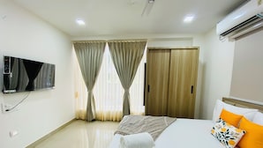 A hotel room with a bed, a TV, a wardrobe, and an air conditioning unit.