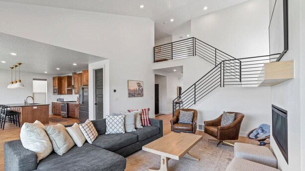 A spacious living area with a grey sectional sofa, a wooden coffee table, and two leather armchairs. A staircase with a black railing leads to an upper level.