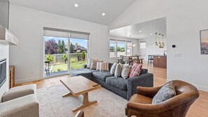 A spacious living room with a grey sofa, wooden coffee table, and leather armchair. A dining area with a wooden table and chairs is visible in the background.