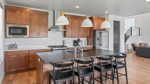 A modern kitchen with wooden cabinets, stainless steel appliances, a central island with bar stools, and pendant lighting.
