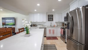 A modern kitchen with white cabinets, stainless steel appliances, a dining area with a table and chairs, and a flat-screen TV. - Fully Furnished Sandy Home | Monthly Stays (Sandy)