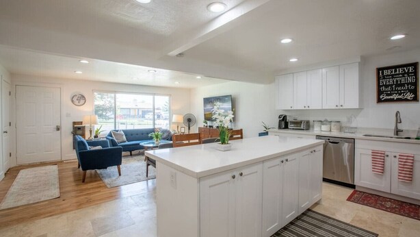 A modern kitchen with white cabinets, a large island, and a dining area with a blue sofa. - Fully Furnished Sandy Home | Monthly Stays (Sandy)