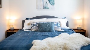 A bedroom with a bed, two bedside tables, a wall-mounted lamp, and a floral artwork. - Fully Furnished Sandy Home | Monthly Stays (Sandy)