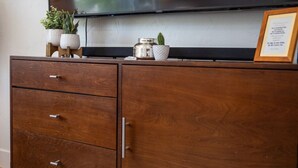 A wooden cabinet with three drawers, a flat-screen TV mounted above, and decorative items including a cactus and a framed picture. - Fully Furnished Sandy Home | Monthly Stays (Sandy)