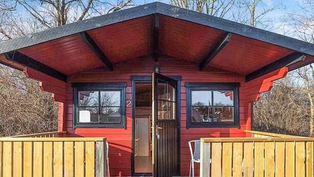 A red cabin with a black roof, a wooden deck, and a door leading inside. - 4 Person Holiday Park Home in Gorlev (Gørlev)