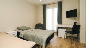 Une chambre à coucher comprenant un lit, un bureau, une chaise, un téléviseur et une fenêtre avec des rideaux.