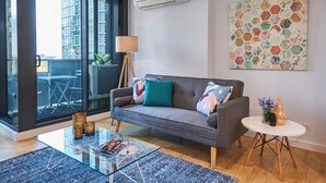A modern living room with a grey sofa, a glass coffee table, and a round side table with a vase.