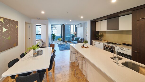 A modern kitchen with a white countertop, stainless steel sink, and bar stools.