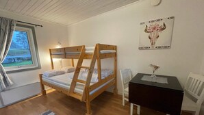 Una habitación con literas, un escritorio, una silla, una ventana con cortinas y un cuadro en la pared.