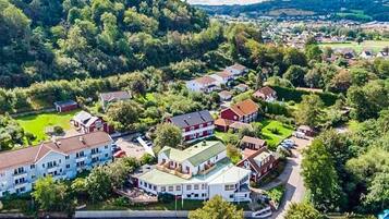 Ett flygbildsbild av ett bostadsområde med hus, grönområden och en kuperad bakgrund.