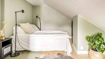 Ett sovrum med en säng, sänglampor, ett litet bord, en växt och en matta.