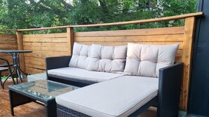 Ein Korbsessel mit Kissen und ein Tisch mit Glasplatte auf einer Terrass.