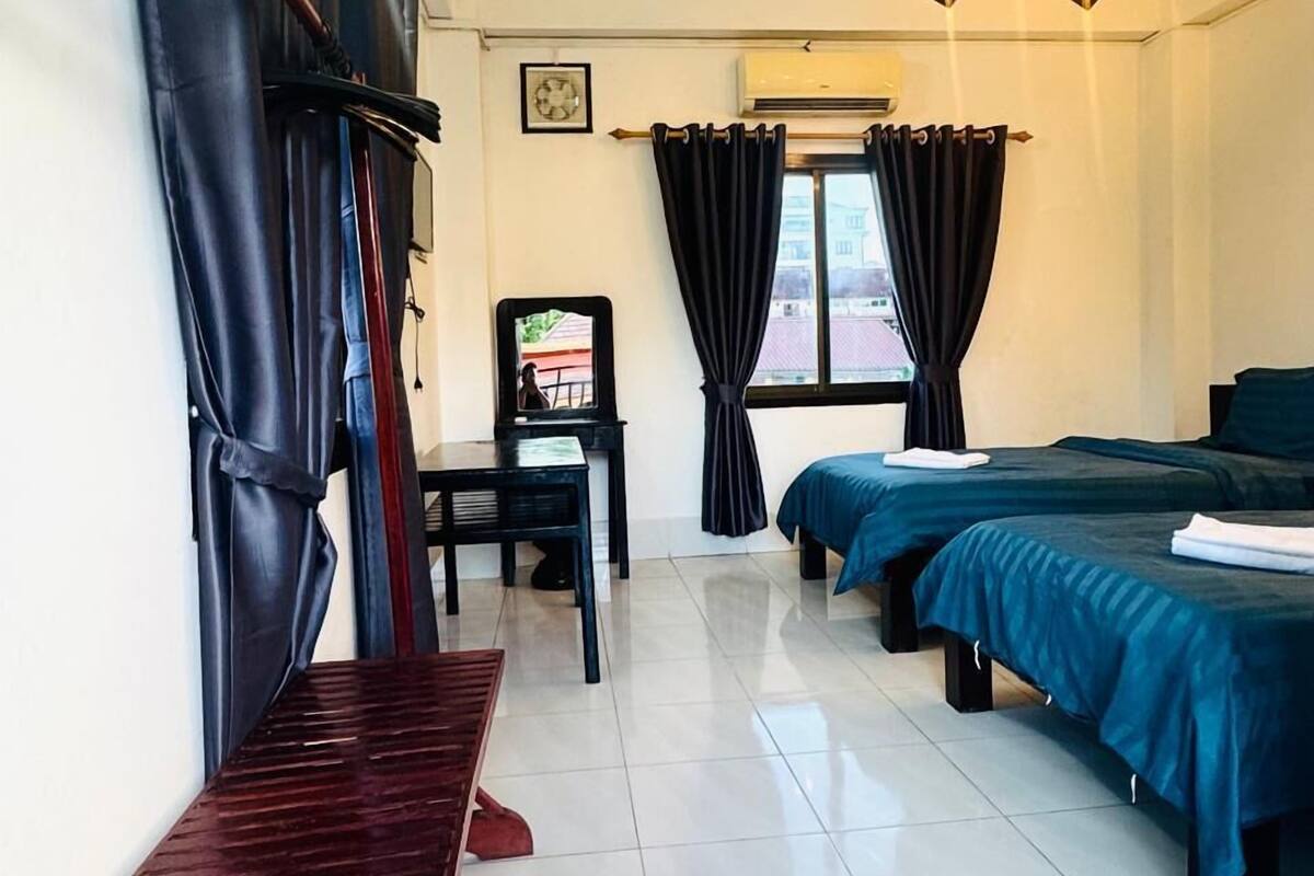 A hotel room with two beds, a piano, a desk, and a staircase.