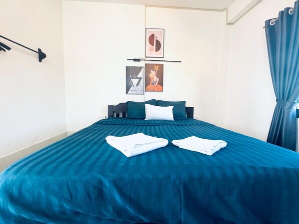Un lit bien fait, avec une couvre-lit bleue et des serviettes blanches, une tête de lit noire et deux tableaux encadrés accrochés au mur.