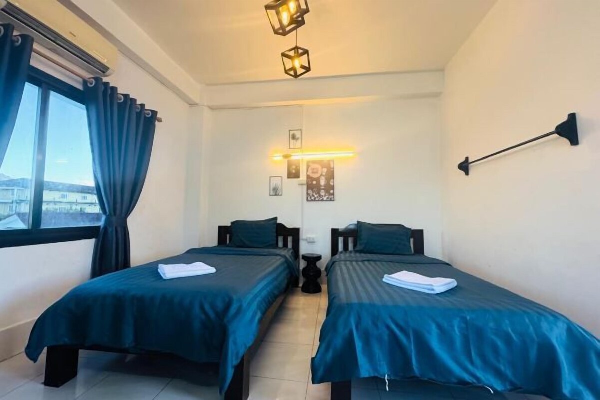 Une chambre d’hôtel avec deux lits simples, une fenêtre avec des rideaux, une lampe fixée au mur et un luminaire au plafond.