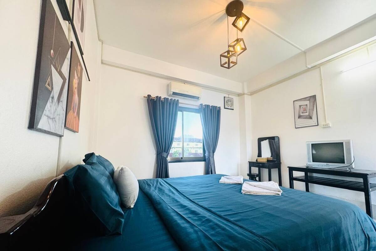 A hotel room with a bed, a desk with a television, and a window with curtains.