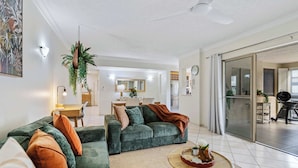A living room with a sofa, coffee table, and a dining area in the background. - Stylish Lakeside Apartment with Spa and Pool View (Cairns North)