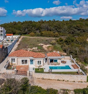 Uma casa grande com piscina, cercada por um muro de pedra e um jardim.