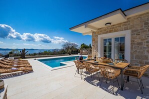 Uma área à beira da piscina com uma mesa e cadeiras, um edifício de pedra e vista para o mar.