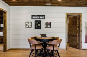 A room with a wooden ceiling, a sign reading 'Welcome to our GAME ROOM,' and a table with chairs.