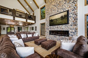 Un salón espacioso con chimenea de piedra, sofás de cuero y un techo alto con vigas a la vista.