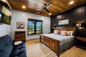 Un dormitorio con techo de madera, una cama con cabecera, una ventana con persianas y obras de arte en las paredes.