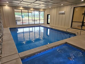 Ein Hallenbad mit klarem Wasser, gefliestem Boden und Blick ins Freie durch groĂe Fenster.