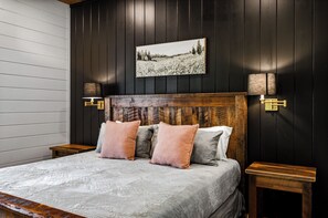 A bedroom with a wooden headboard, a bed with multiple pillows, two bedside tables, and a wall-mounted lamp.