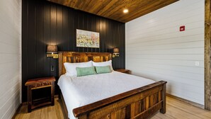 A bedroom with a wooden bed, two nightstands, a painting on the wall, and a ceiling light. - Grand Forge Lodge - 16 Bedrooms in the MIDDLE of Pigeon Forge! Loaded! (Pigeon Forge)