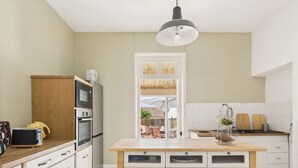 Una cocina moderna con armarios blancos, una isla de madera con cajones, un horno empotrado y una lámpara colgante.
