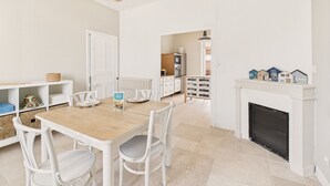 Un interior luminoso y blanco con una mesa de comedor, sillas, una lámpara colgante y una chimenea.