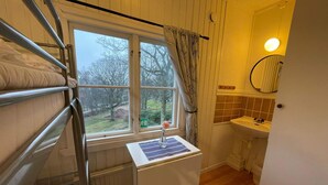 Ein Stockbett mit Fenster, ein kleiner Tisch mit einem Laptop, ein Waschbecken und ein Spiegel in einem Raum mit Holzboden.
