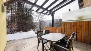An outdoor patio with a table and chairs, a wooden fence, and a view of a snowy landscape. - Apartment in Hotting Near Nordkette (Innsbruck)