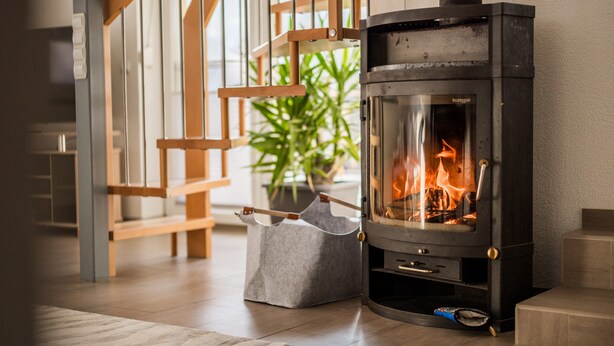 A modern living room with a wood-burning stove, a grey storage basket, and a wooden bench. - Apartment in Hotting Near Nordkette (Innsbruck)