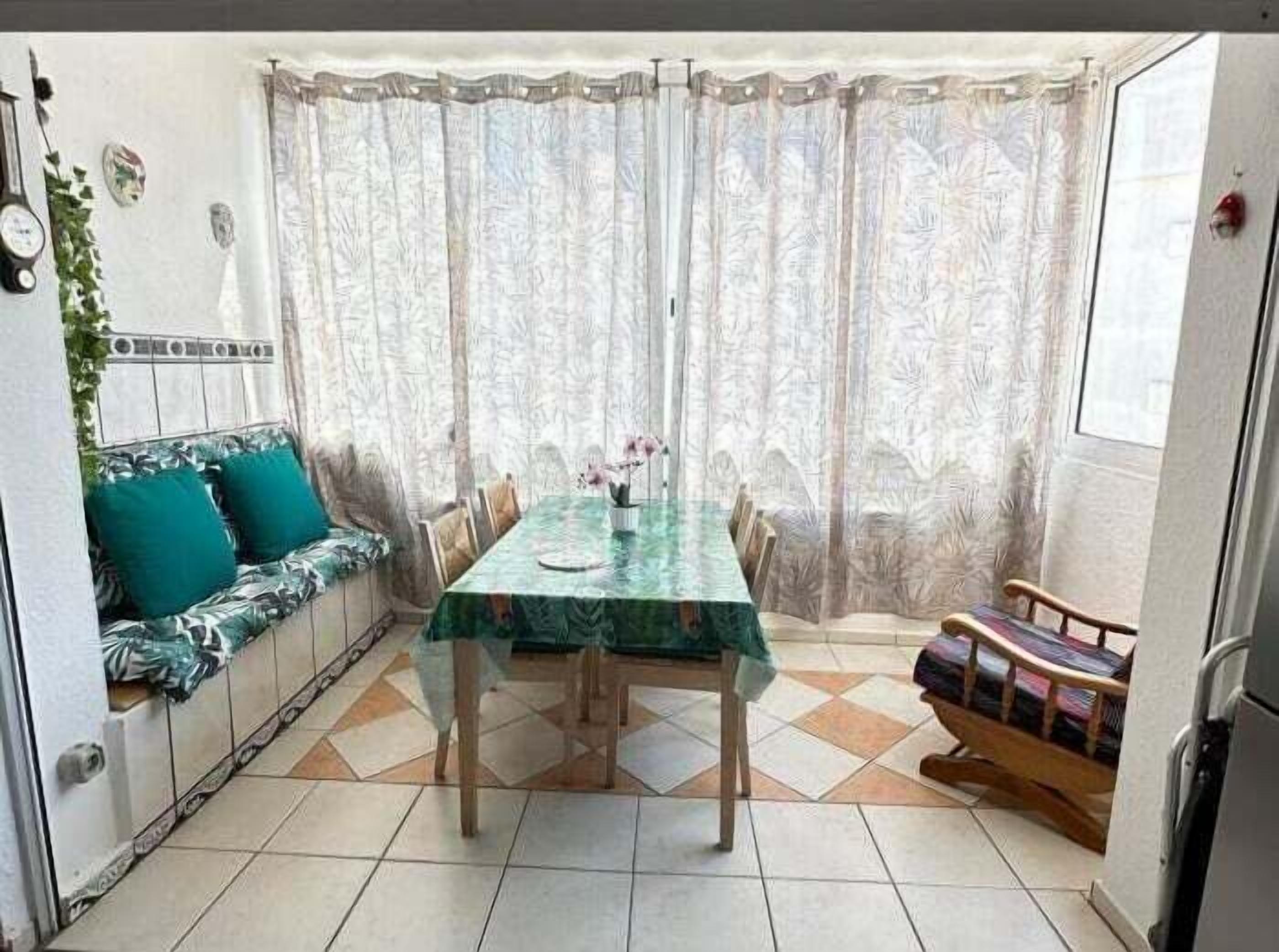 A dining area with a table, chairs, a sofa with cushions, and a window with curtains.