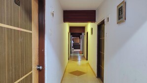 A narrow hallway with a tiled floor, a wooden door on the left, and a framed picture on the right. - Hotel Kolkar (Panvel)