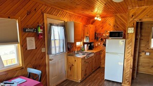 A wooden cabin kitchen with a dining area, a refrigerator, and a microwave. - Schurman’s Shore Cottage #3 (Travellers Rest)