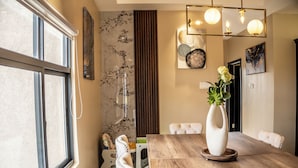 Ein Essbereich mit einem Holztisch, weißen Stühlen, einer Blumenvase und Bildern an den Wänden.