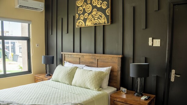Ein ordentlich eingerichtetes Schlafzimmer mit einem Bett, Nachttischlampen, einem Holfnachtkästchen und einem Wandbild.