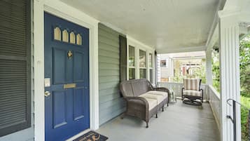 A porch with a blue door, a wicker sofa, and a chair.
